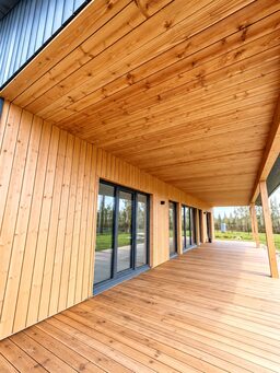 A wooden terrace with large glass doors and a wooden ceiling.