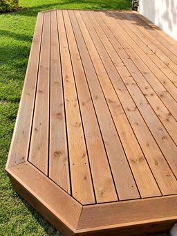 A wooden terrace deck with a smooth surface and a corner edge, set on green grass.