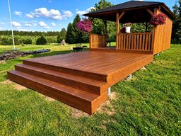 A wooden terrace with steps leading up to a gazebo surrounded by greenery.