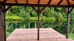 Skats no koka terases uz ūdeni un zaļumiem.